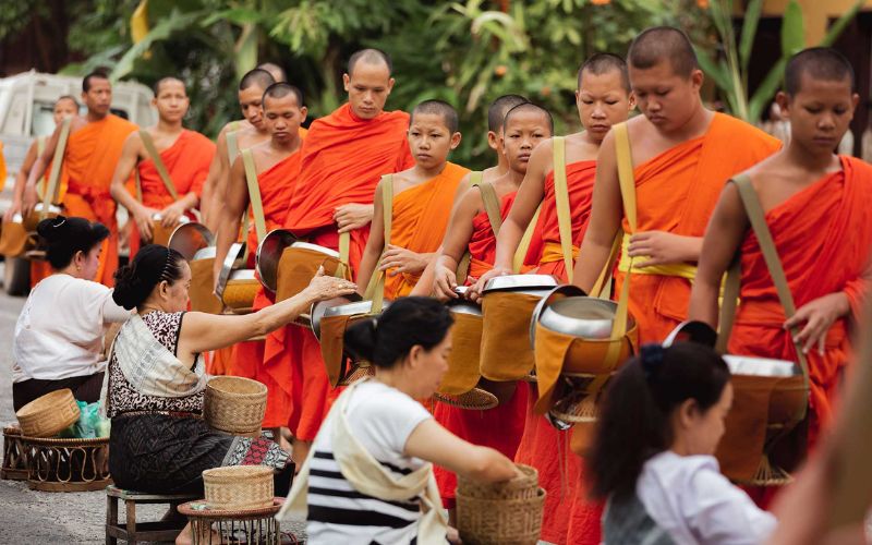 Local people offering food to Buddhist monks during the morning alms-giving ceremony in Laos.