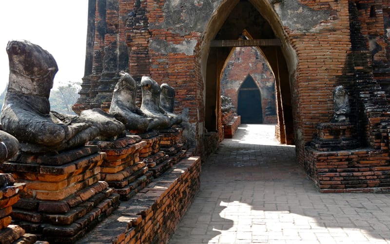 Ancient brick corridor lined with headless Buddha statues at a historic temple ruin in Ayutthaya, Thailand, showing the remnants of the old Siamese kingdom.