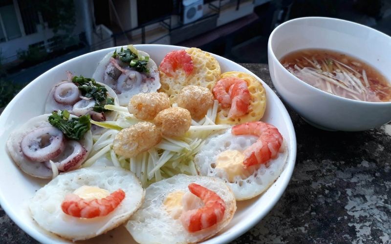 A plate of mini rice pancakes topped with shrimp, quail egg, and squid, served with dipping sauce in Nha Trang, Vietnam.