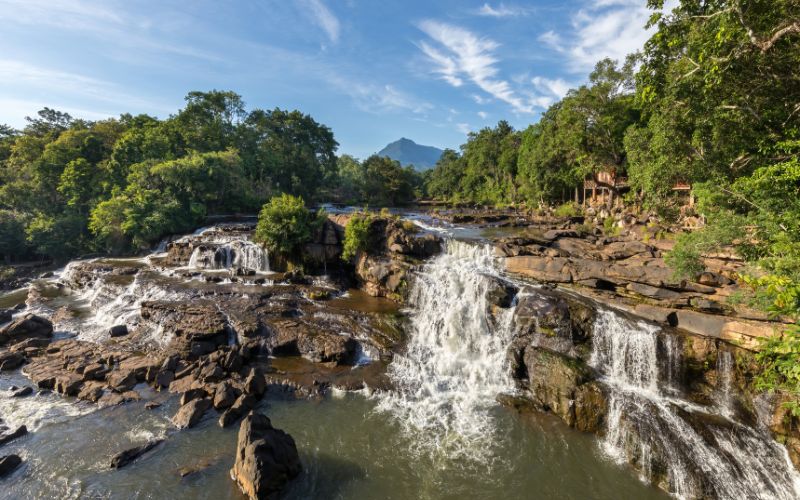 Waterfall flowing over rocky terrain surrounded by lush greenery on the Bolaven Plateau, Laos