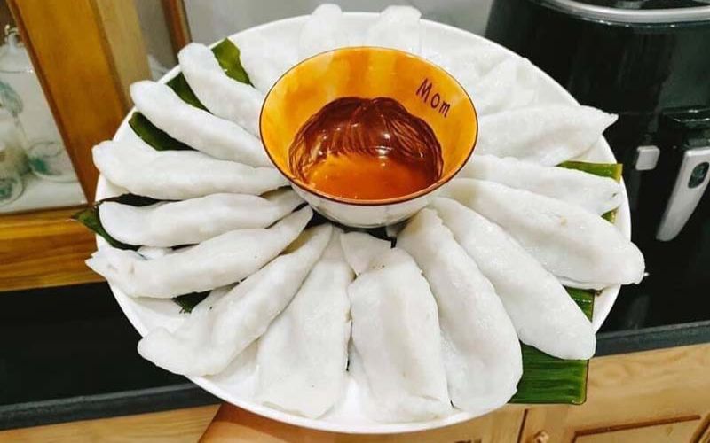Plate of Banh Tai dumplings arranged in a circle around a bowl of dipping sauce, served on banana leaves.
