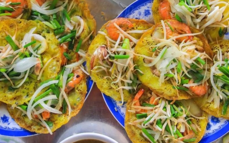 Crispy Vietnamese pancakes filled with squid, shrimp, and bean sprouts, served on blue and white plates.
