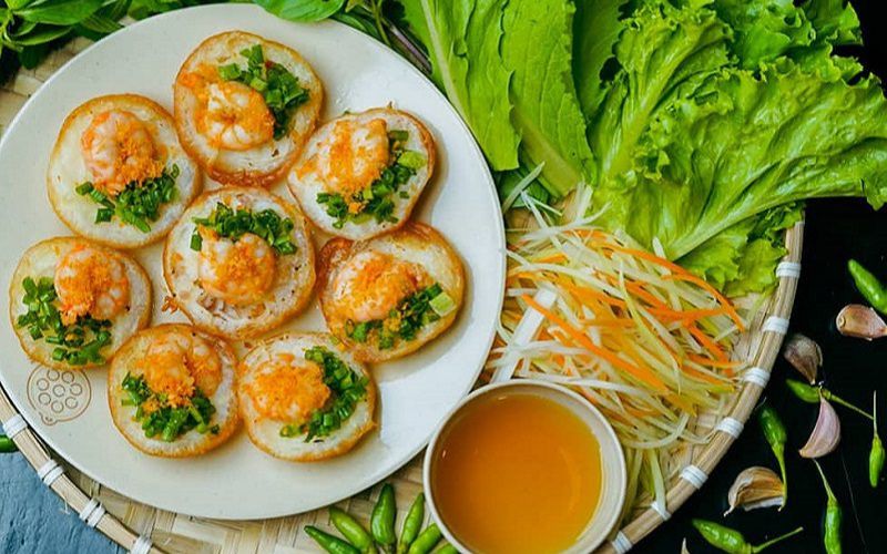 Traditional Banh Can Cham pancakes with shrimp topping, served with fresh herbs and dipping sauce in Ninh Thuan, Vietnam