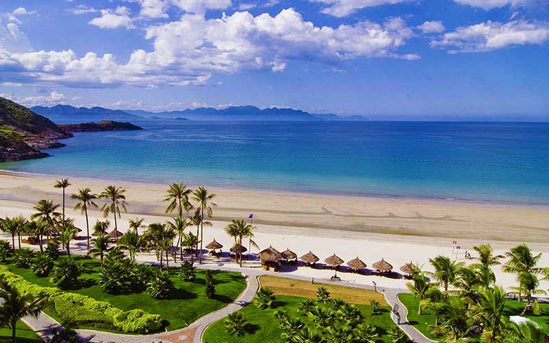 Wide stretch of golden sand at Back Beach, Vung Tau, with gentle waves, palm-lined promenade under the clear blue sky