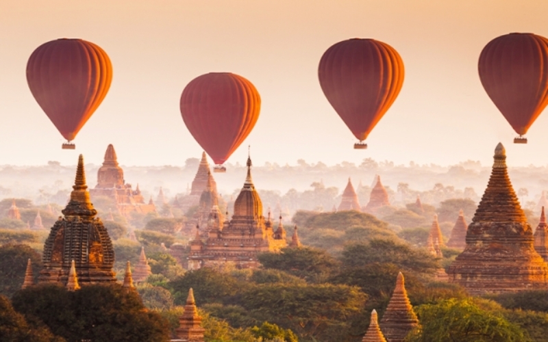 Colorful hot air balloons floating above Bagan’s temples at sunrise, with layers of mist over the plains.