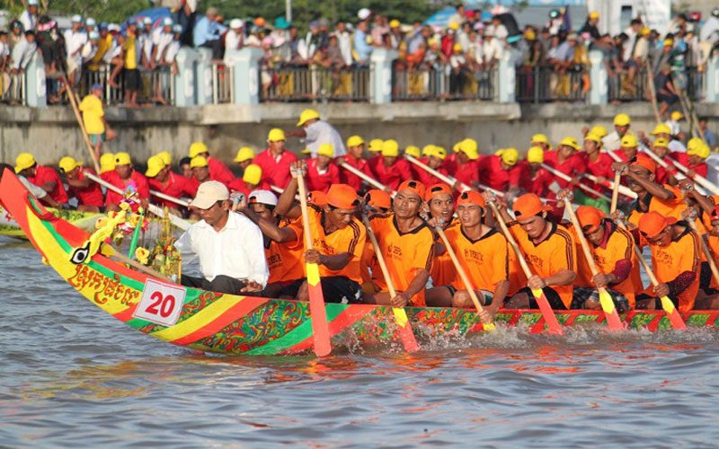 Rowers in colorful uniforms paddling a long dragon boat during the Bon Om Touk water festival in Cambodia.
