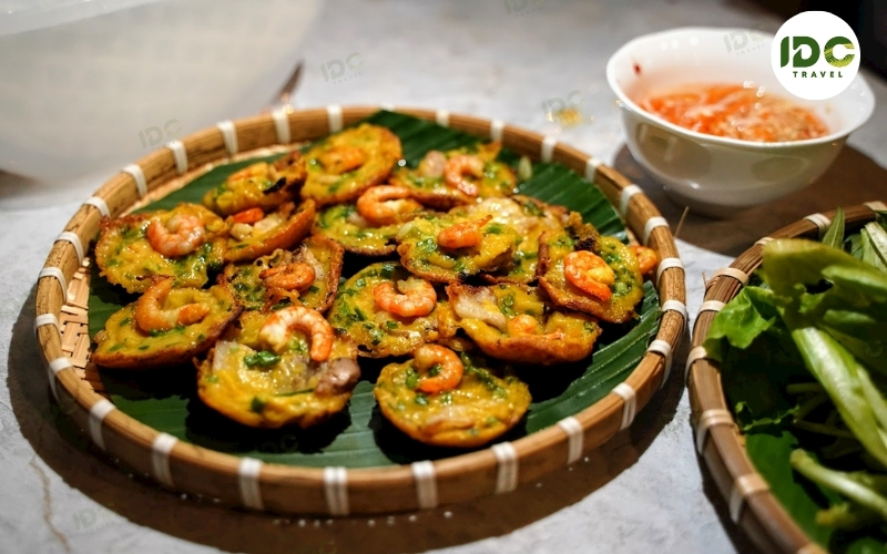A plate of banh khot, mini savory Vietnamese rice pancakes topped with shrimp, served with fresh herbs and dipping sauce.