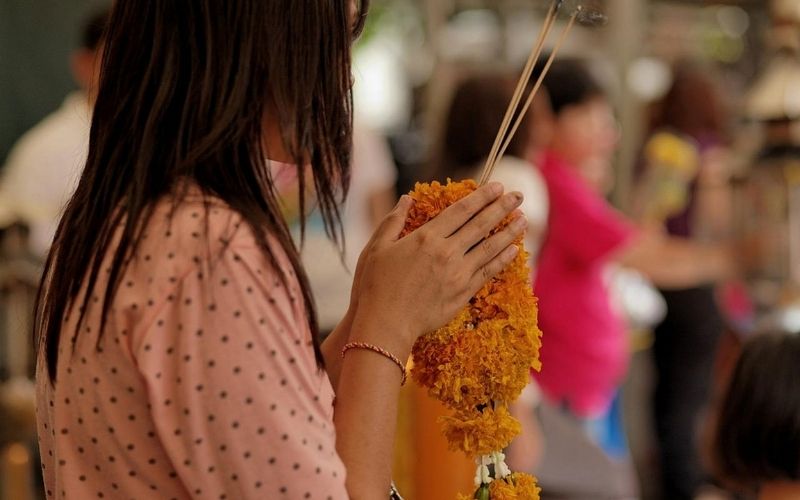 Woman holding incense sticks and flower offerings during a Buddhist ritual at a temple in Luang Prabang, Laos.