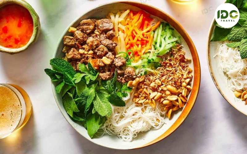 A bowl of bun thit nuong, Vietnamese grilled pork noodle salad with rice vermicelli, herbs, carrots, and crushed peanuts.