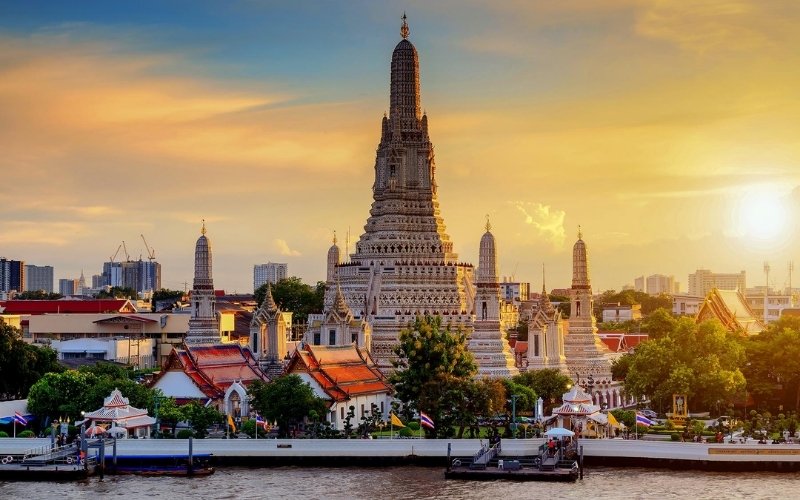 Stunning view of Wat Arun temple in Bangkok, Thailand, with intricate architecture illuminated by the golden glow of sunset, reflecting on the Chao Phraya River.