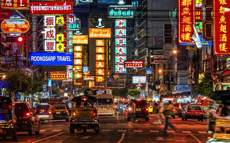 Night view of Yaowarat Road filled with cars, food stalls, and glowing neon signs.