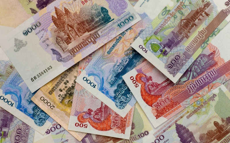 several Cambodian banknotes in different denominations, including 100, 500, 1,000, and 2,000 Riel. The colorful notes feature images of Angkor Wat, traditional architecture, and cultural symbols of Cambodia.