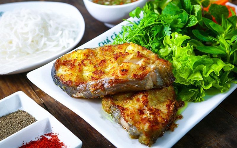 Grilled Ca Lang fish from the Lo River, served with fresh herbs, vermicelli noodles, and dipping sauces on a white plate