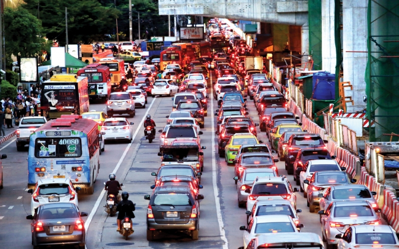 Vehicles of all kinds, cars, tuk-tuks, and motorbikes, navigate a busy, signal-free intersection in central Bangkok, reflecting the city’s fast-paced and unpredictable traffic flow.