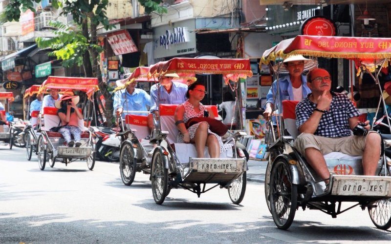 Tourists enjoy a traditional cyclo ride through the vibrant streets of Hanoi’s Old Quarter, passing colorful shop signs, local art galleries, and the everyday buzz of city life, a nostalgic and relaxing way to explore the charm of the city at street level.