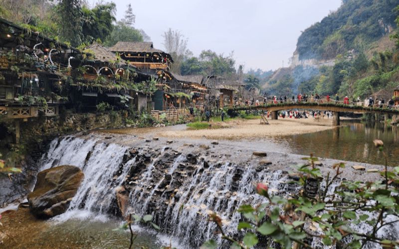 Cat Cat Village in Sapa, Vietnam, with a small waterfall, wooden houses, and a footbridge surrounded by mountain scenery.