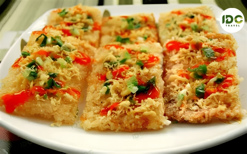 Sliced com chay Ninh Binh, crispy Vietnamese scorched rice, topped with shredded pork floss, scallions, and chili sauce, served on a white plate.