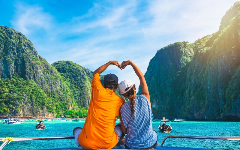 A couple enjoys a romantic moment on a boat, surrounded by the stunning turquoise waters and towering limestone cliffs of the Phi Phi Islands in Phuket.
