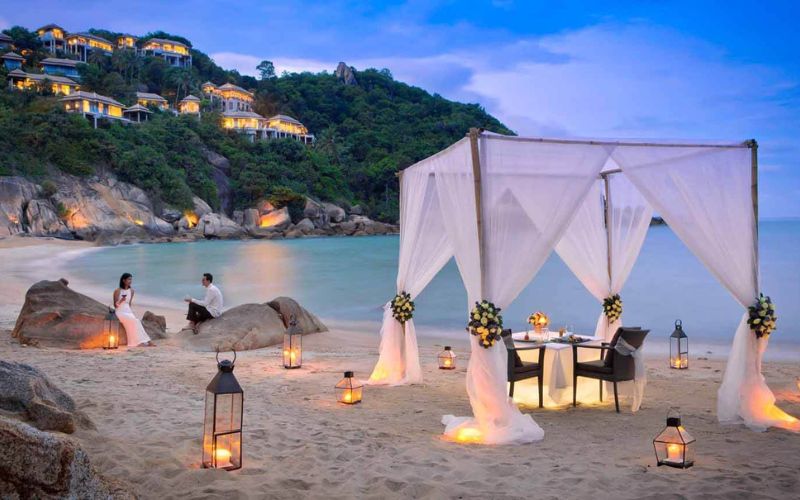 Romantic beachside dinner setup for a couple’s honeymoon in southern Thailand, with lanterns and ocean views at sunset