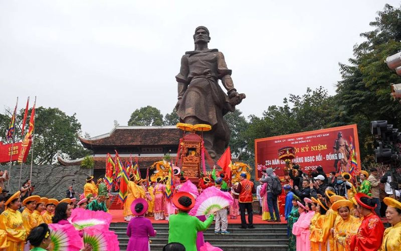 Dong Da Hill Festival celebration in Hanoi featuring traditional dancers in yellow and pink áo dài performing before the statue of Emperor Quang Trung at the Dong Da Mound.
