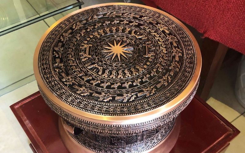 A collection of ancient Dong Son bronze drums with intricate geometric patterns on display in a museum gallery.