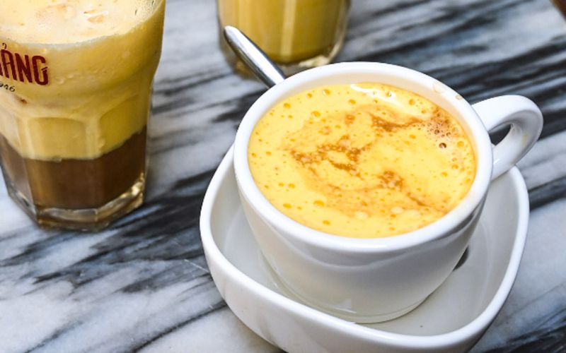 A cup of Giang egg coffee with a creamy golden foam, served in a white cup on a marble table