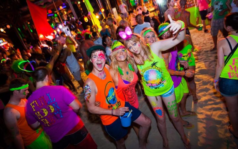 Partygoers in neon outfits enjoying the vibrant Full Moon Party on the beach at Koh Phangan, Thailand