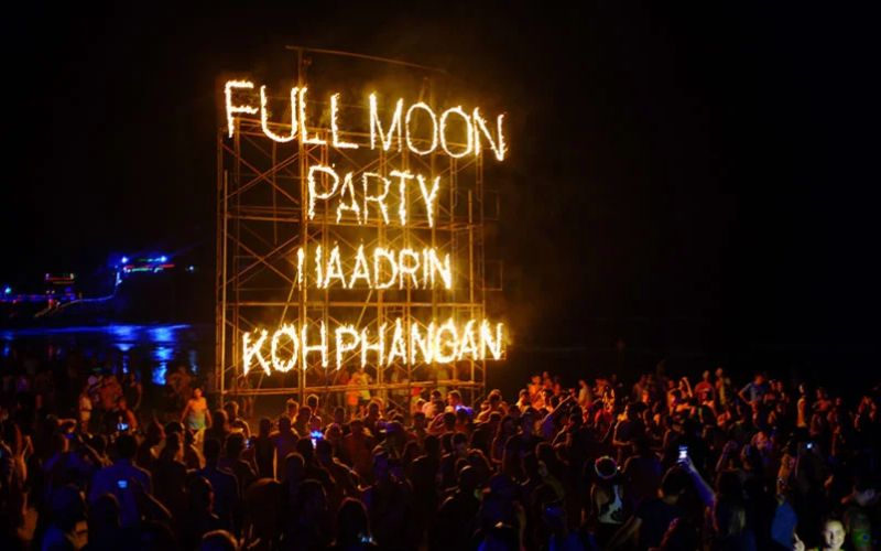 Crowd dancing under neon Full Moon Party sign at Haad Rin Beach, Koh Phangan, Thailand