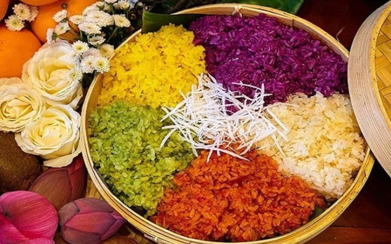 Traditional Vietnamese five-color sticky rice arranged in a round bamboo tray, featuring purple, yellow, green, red, and white glutinous rice with shredded coconut garnish