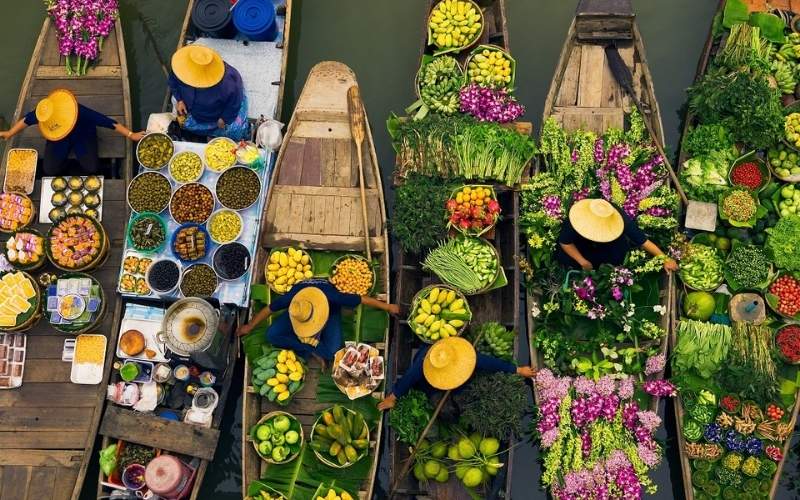 Aerial view of a vibrant floating market in Vietnam with vendors wearing conical hats selling colorful fruits, vegetables, and flowers from wooden boats.