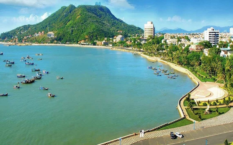 Scenic view of Front Beach in Vung Tau with calm blue waters, boats anchored offshore, and the city skyline in the background.