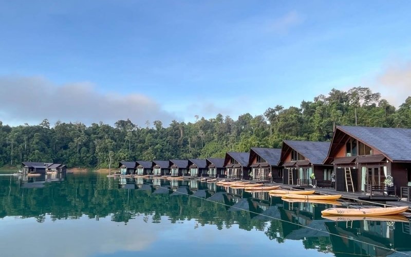 Modern floating bungalows on the calm emerald waters of Cheow Lan Lake in Khao Sok National Park, surrounded by lush rainforest.