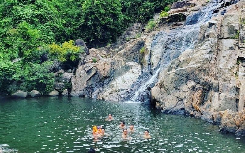 Travelers swimming beneath a hidden waterfall in Son Tra, Da Nang – a serene forest bathing experience in lush natural surroundings