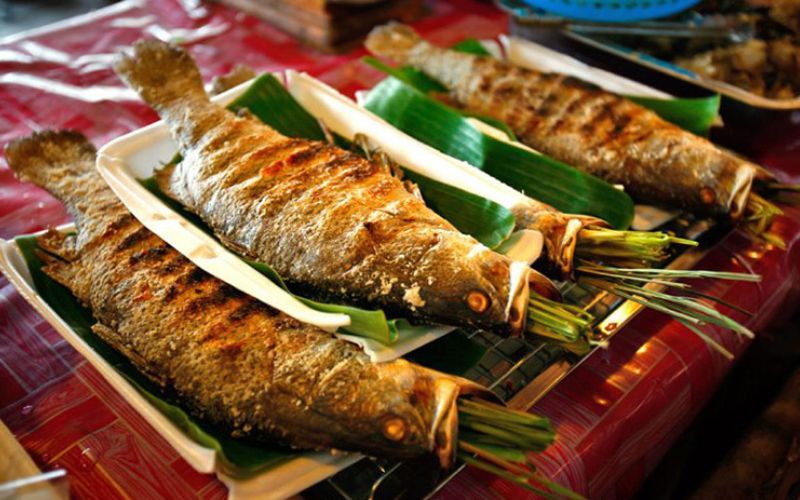 Grilled stream fish served on banana leaves, stuffed with fresh herbs, and displayed on a tray in a traditional Vietnamese style