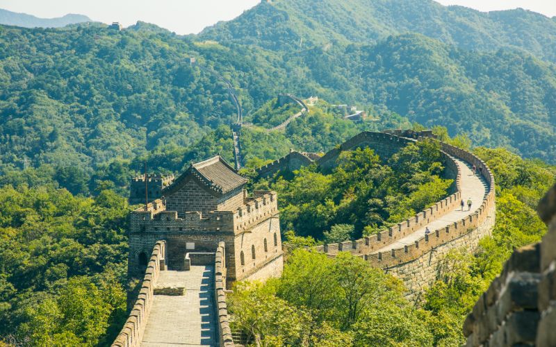 The Great Wall of China winding through lush green mountains under a clear sky
