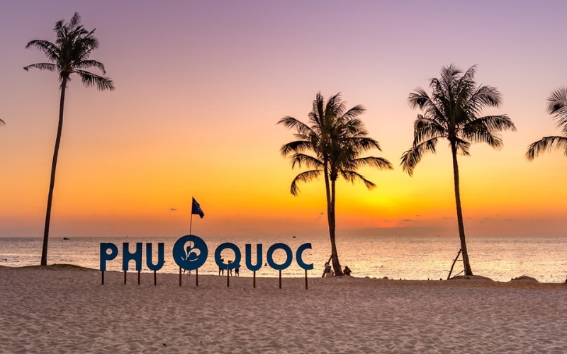 View of the sun dipping below the horizon at Long Beach in Phu Quoc, with golden light reflecting on calm waves and palm-fringed sands.