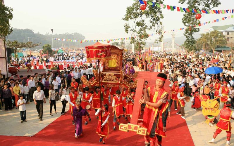 A ceremonial procession at the Giong Festival in Hanoi with local participants carrying a red and gold palanquin and wearing traditional festival costumes on a red carpet.