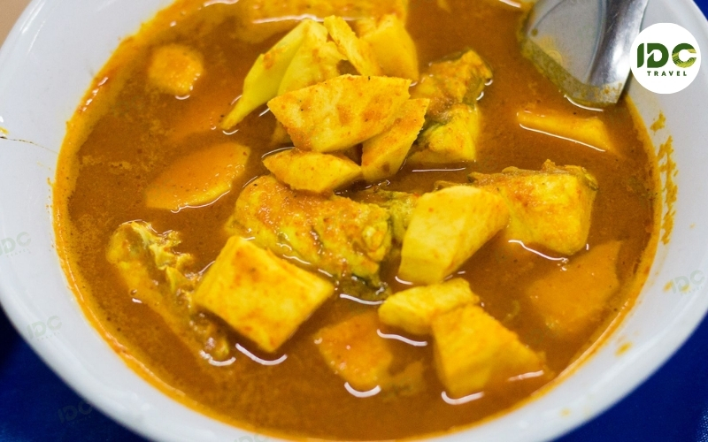 A bowl of gaeng som pla, Thai sour fish curry with fish and vegetables in an orange broth.