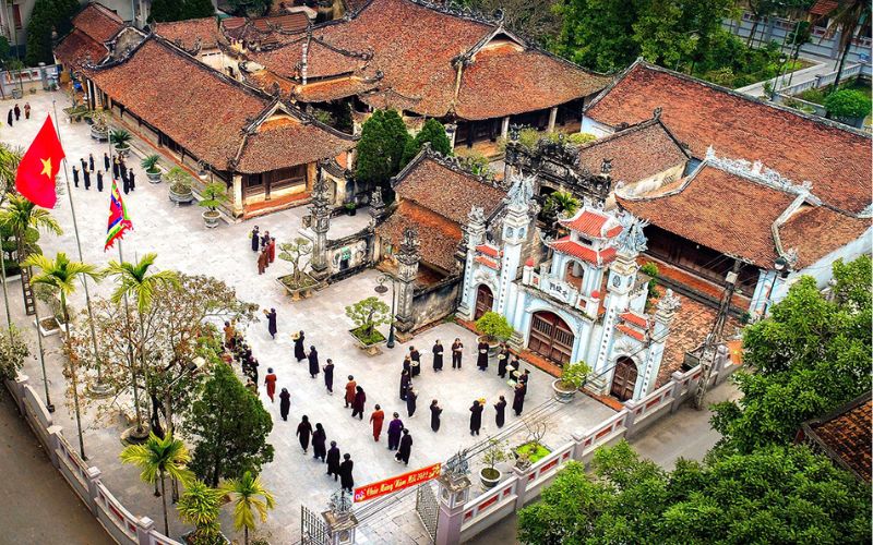 Aerial view of Hung Lo Ancient Village in Phu Tho, Vietnam, featuring traditional red-tiled houses, a village gate, and people gathering in the courtyard
