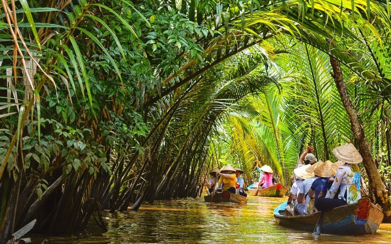 Tourists rowing through palm-lined canals on the Ham Luong River in Ben Tre, Vietnam, showcasing the charm of the Mekong Delta