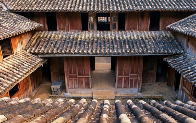 Traditional Hmong King Palace in Ha Giang, Vietnam, featuring stone walls, wooden doors, and intricate carvings, surrounded by lush green mountains.
