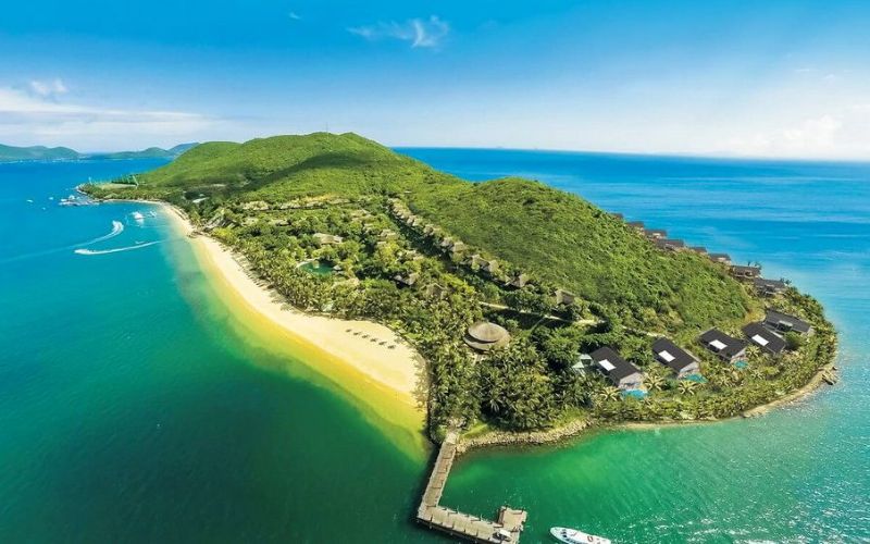 Aerial view of Hon Tre Island near Nha Trang featuring a long sandy beach, turquoise water, green hills, and resort villas along the coastline.