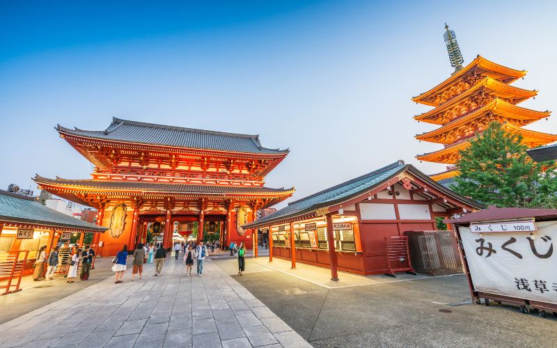 Senso-ji Temple in Tokyo, Japan, with visitors walking near the illuminated gate and five-story pagoda at dusk