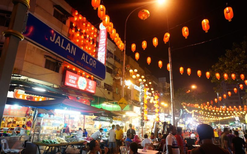 Night scene at Jalan Alor in Kuala Lumpur, Malaysia, showcasing bustling street food stalls, glowing lanterns, and lively crowds enjoying local cuisine