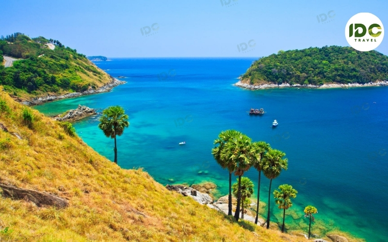 Aerial view of the headland at Nai Harn, Phuket, Thailand, with palm trees, blue bays, and boats anchored offshore.