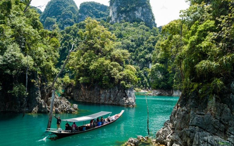 Long-tail boat on emerald water surrounded by limestone cliffs at Khao Sok National Park, Thailand