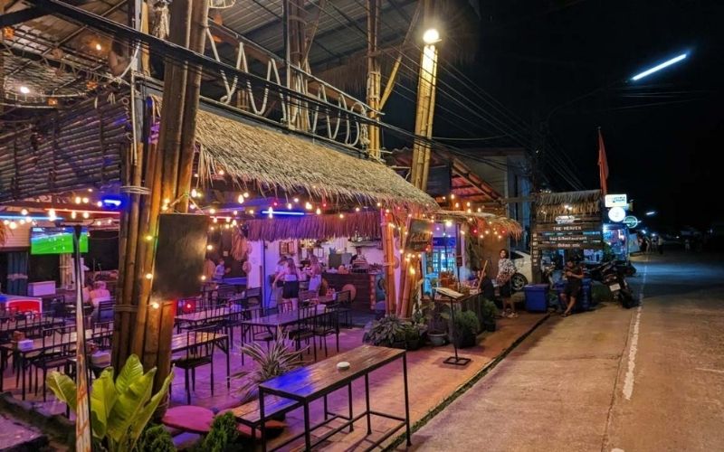 Cozy open-air restaurant with bamboo décor and colorful string lights in Khao Sok Village, Thailand, offering a relaxed evening atmosphere.