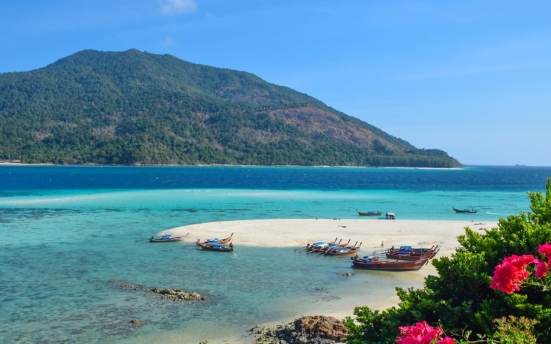 Koh Lipe, Thailand, showing turquoise waters, coral reefs, and white sandy beaches surrounded by lush greenery.