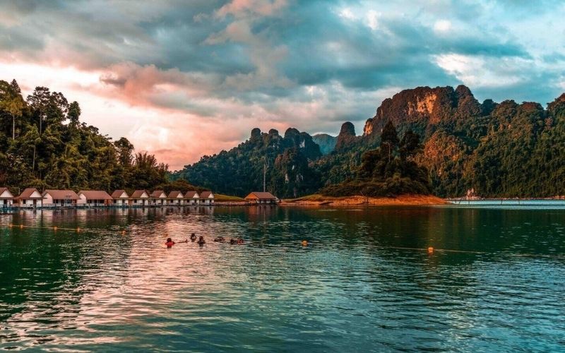 Scenic view of floating bungalows on Cheow Lan Lake in Khao Sok National Park, Thailand, surrounded by limestone mountains and lush rainforest at sunset.