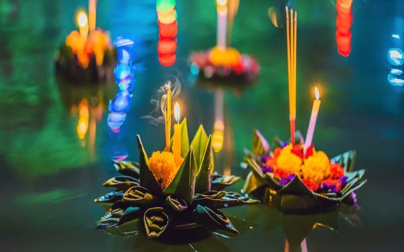 Close-up of beautifully decorated Krathongs made from banana leaves and flowers, floating on water with candles and incense sticks during Thailand’s Loy Krathong Festival.